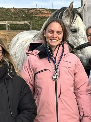 Dr Anne-Claire Idoux, stéthoscope autour du cou, devant un cheval gris